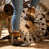 Women wearing a brass and silver botin with a riding cowboy on the outer par of the shaft and studs.