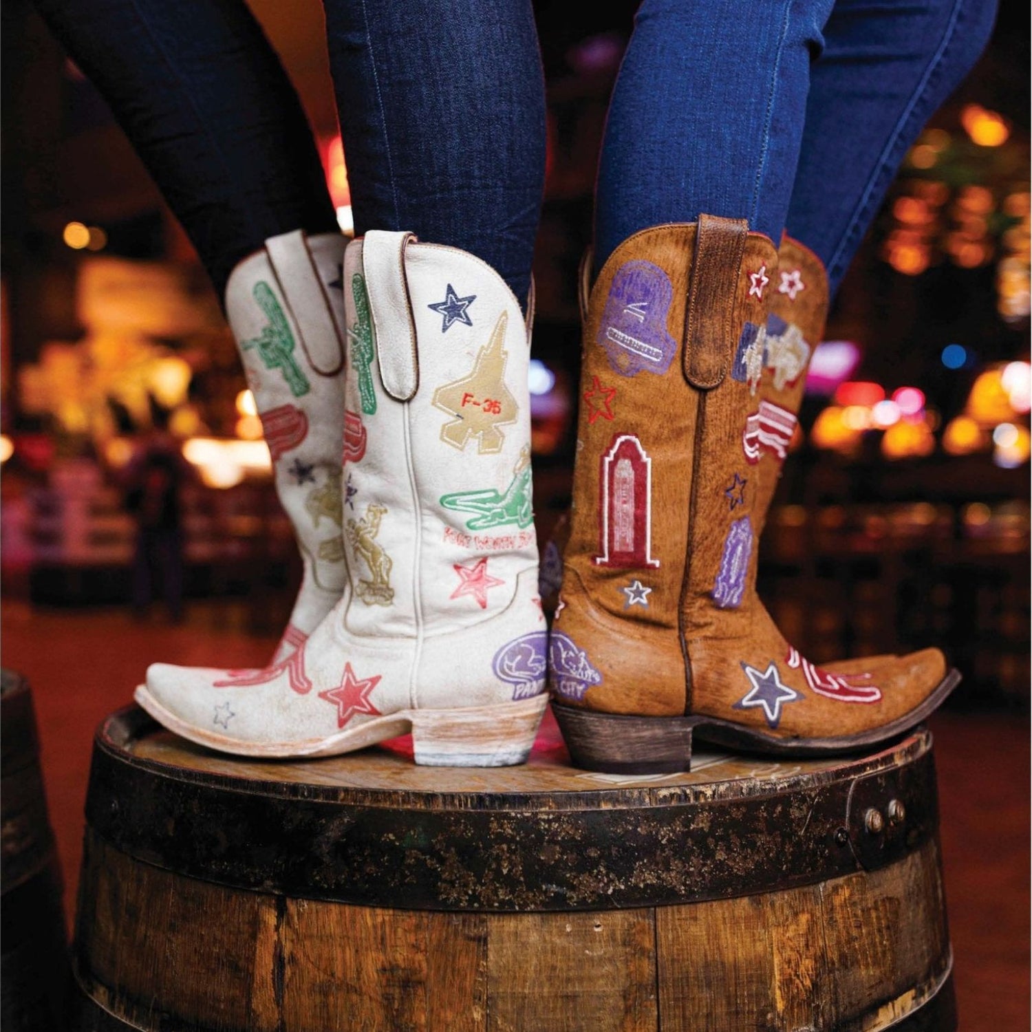 Two pairs of cowboy boots with colorful designs on a barrel, blurred background